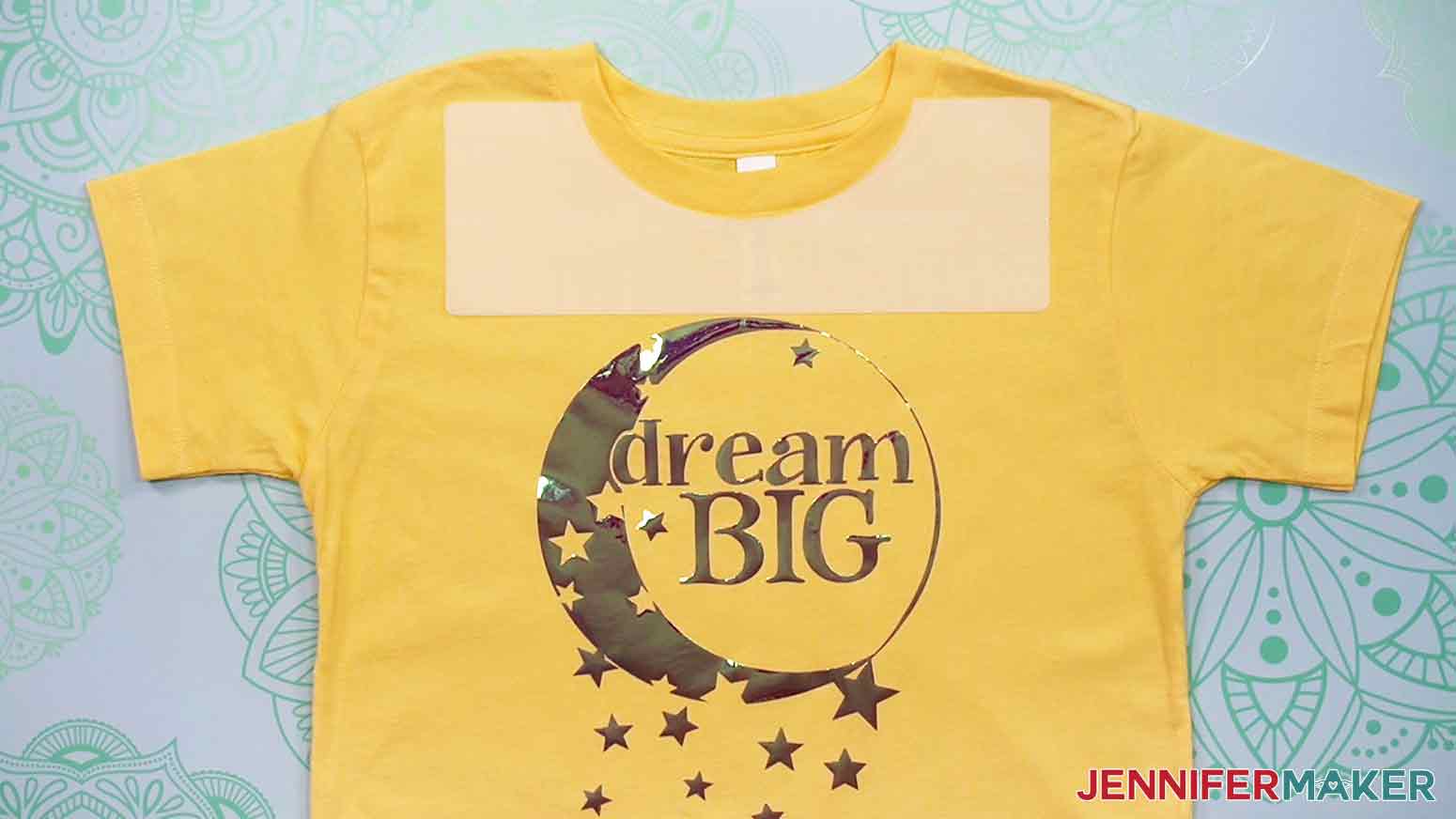 Here is an example of a yellow, youth-size crew-neck T-shirt with the plastic Youth T-Shirt Ruler aligned under the neckline of the shirt, showing the proper placement and spacing of the Dream Big decal.