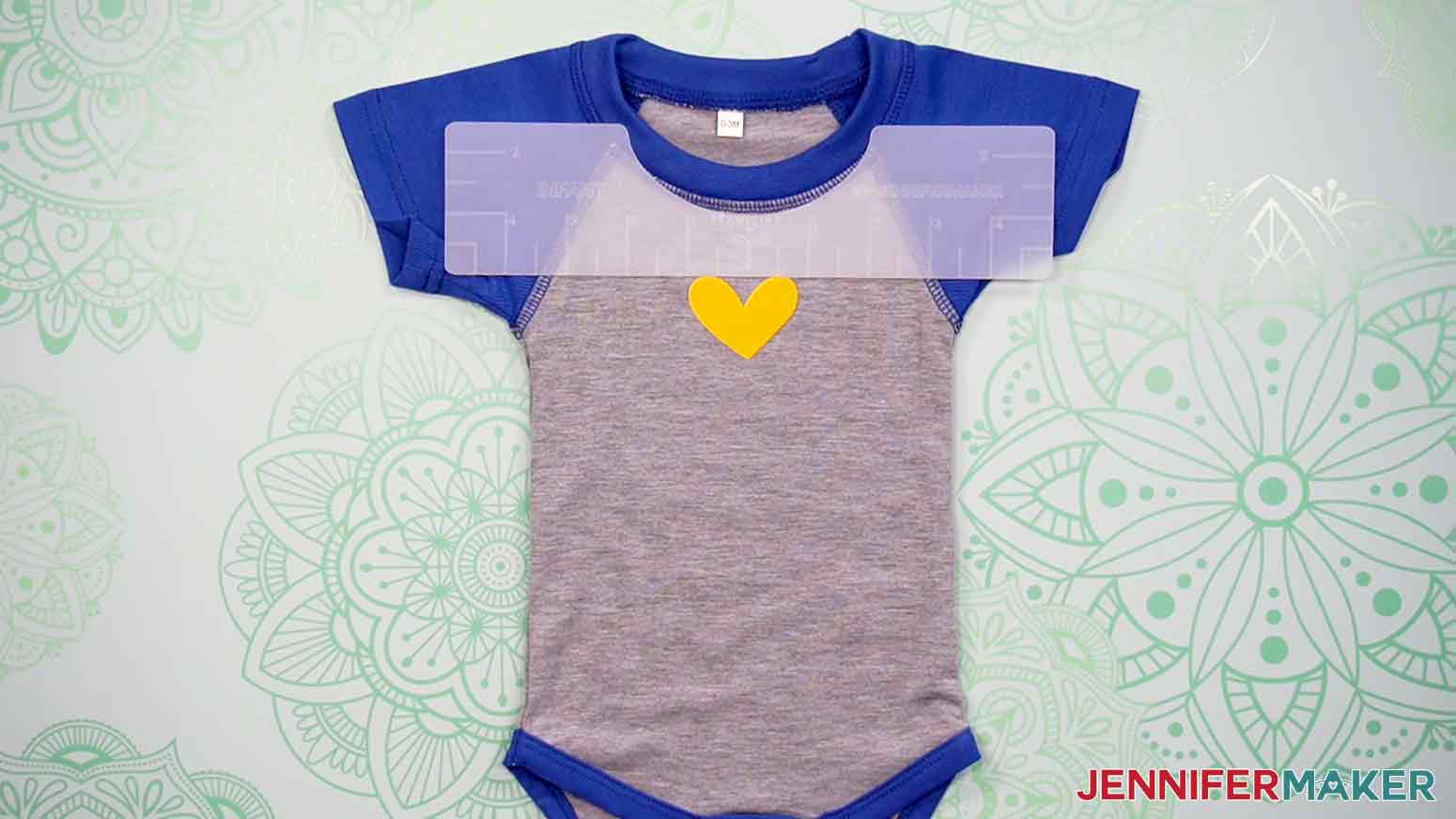 Here is an example of a grey and blue, infant onesie, with the plastic Infant T-Shirt Ruler aligned under the neckline of the onesie, showing the proper placement of a yellow heart decal.