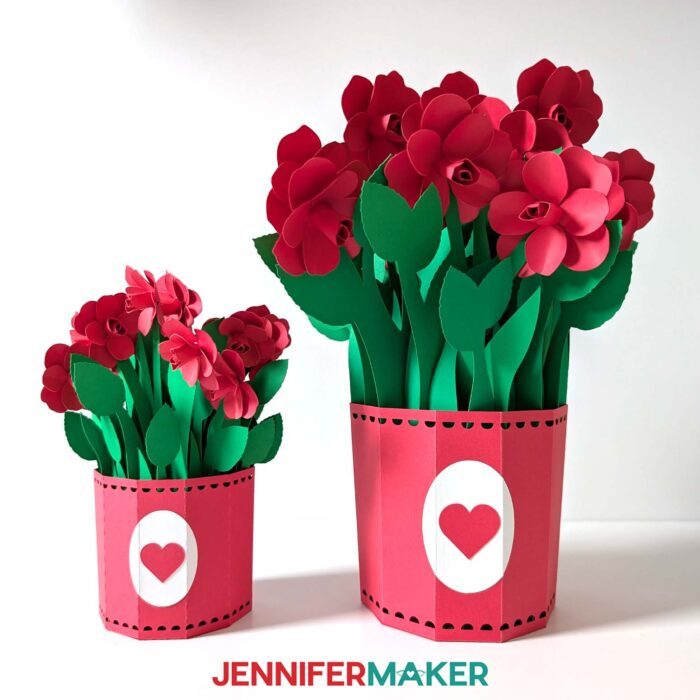 Two matching 3D Pop-Up Spring Flowers bouquets with red pots and red roses. One pot is a small version cut with a Cricut Joy, and the other is the full-size version for other cutting machines