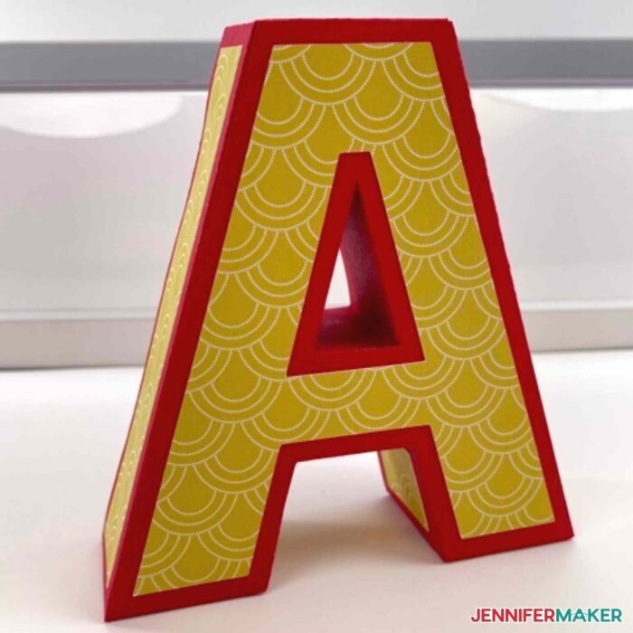 A 3D Paper Letter A box with yellow and white patterned accents and red edges standing on a white table.