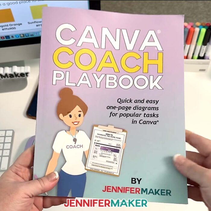 Hands hold a purple and blue book titled "Canva Coach Playbook: Quick and Easy One-Page Diagrams for Popular Tasks in Canva" by JenniferMaker. Learn more about it in my Best Canva Tools For Business video