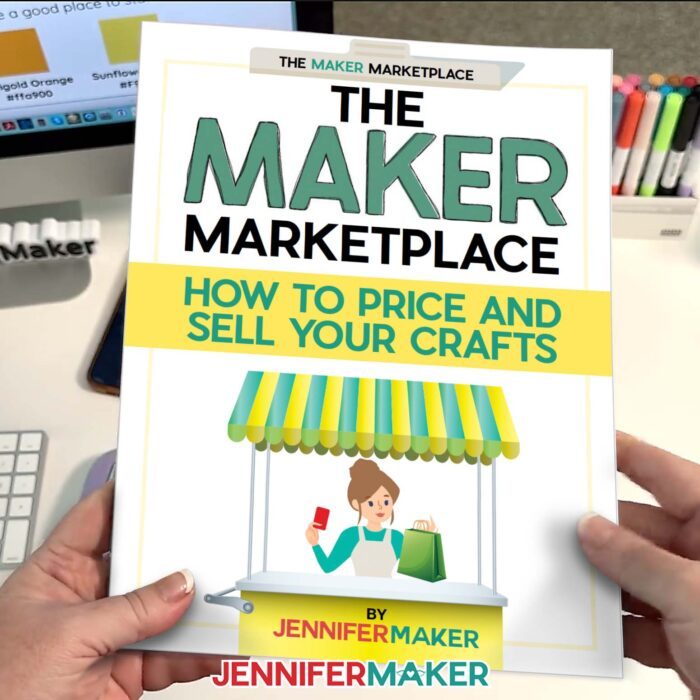 Hands hold a green and white book titled "Maker Marketplace: How to Price and Sell Your Crafts" over a white desktop. Get a free sample excerpt in my post Best Canva Tools For Business