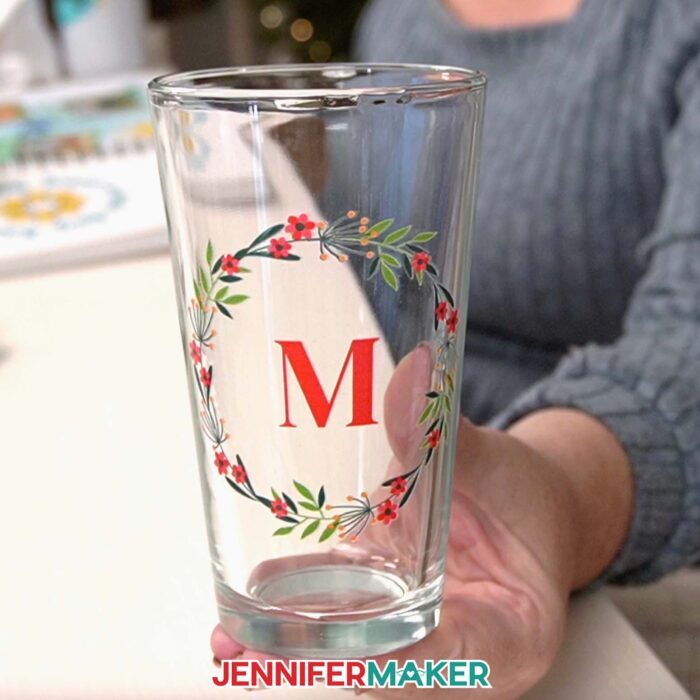 A close-up of a glass tumbler Canva gift. It has a wreath design with a red letter M in the center printed on it.