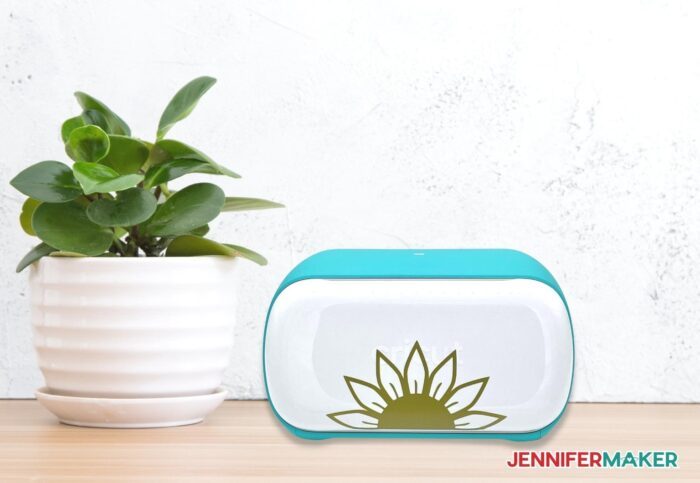 A Cricut Joy machine with a gold vinyl sunflower design on its front door, sitting on a desk.