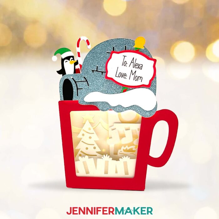 Red Hot Chocolate Shadow Box with a layered Christmas tree scene inside with gifts, and a sparkly cardstock igloo and penguin with a candy cane top, with a sign saying "To: Alexa, Love: Mom"