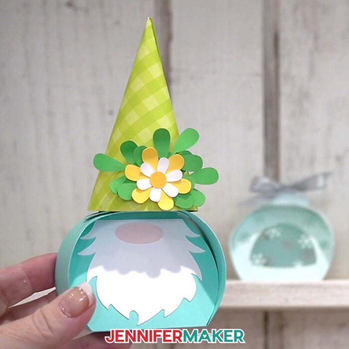 A hand shows off the gnome box from the Curvy Keepsake Boxes tutorial, with the snowflake box in the background