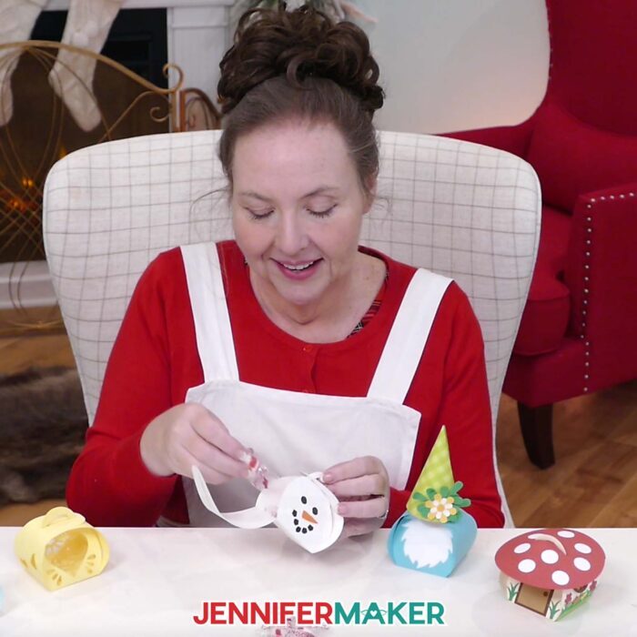 Jennifer Maker sits at her craft table, showing off Curvy Keepsake Boxes and assembling the snowman box