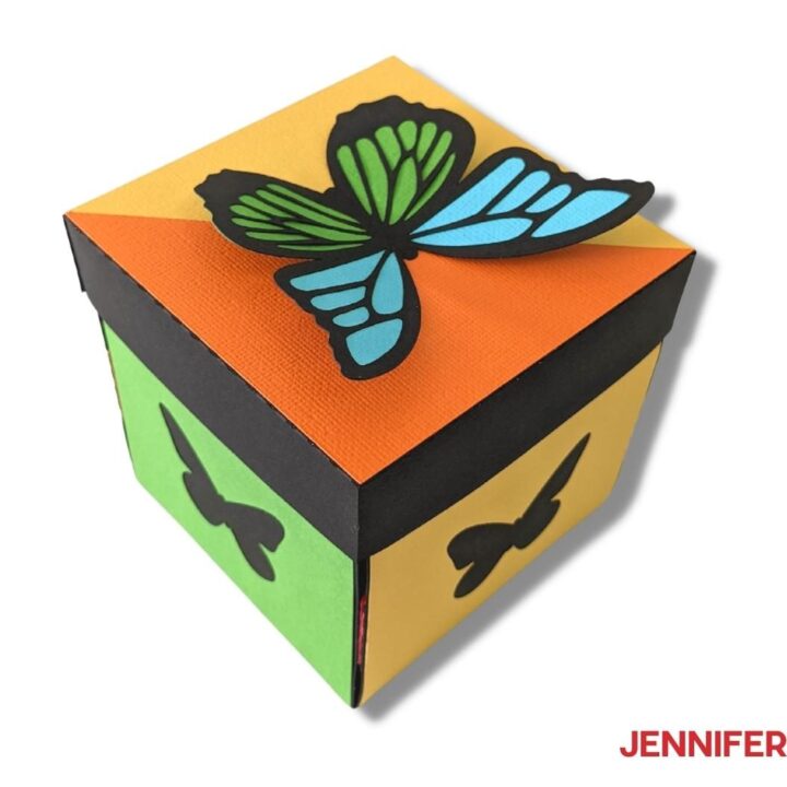 A square decorative DIY exploding butterfly box made with colorful cardsock and topped with a 3D butterfly.