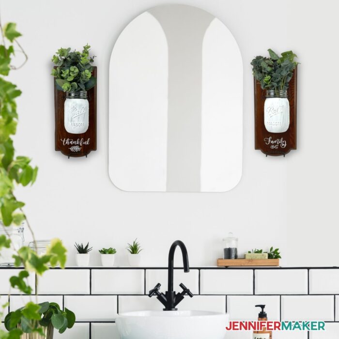 DIY Mason Jar Wall Decor on the sides of a mirror with a sink below it and some greenery