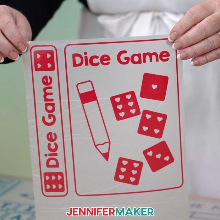 Learn how to make a DIY Board Game Box to store all your game pieces with JenniferMaker's tutorial! Jennifer holds up heat transfer vinyl labels and decals for a Dice Game book box.
