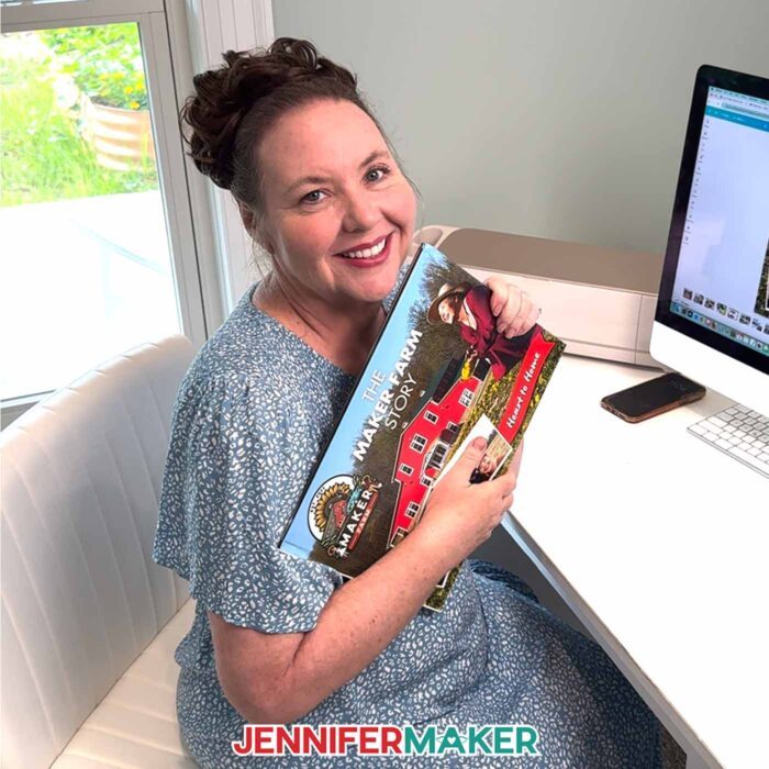 Jennifer Maker sits at her computer desk and hugs her DIY Photo Book she created with Canva
