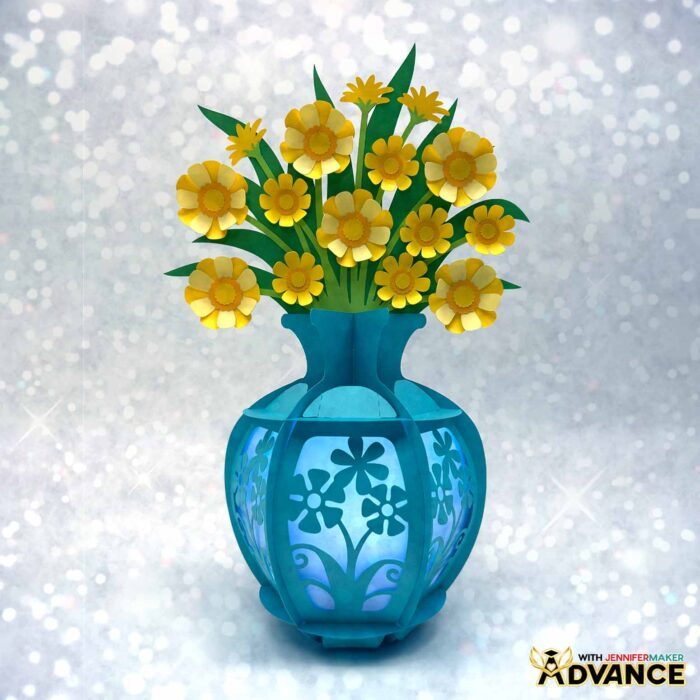A blue lantern with custom cardstock panels and a bouquet of yellow and white flowers. Learn how to customize this design in Advance with JenniferMaker!
