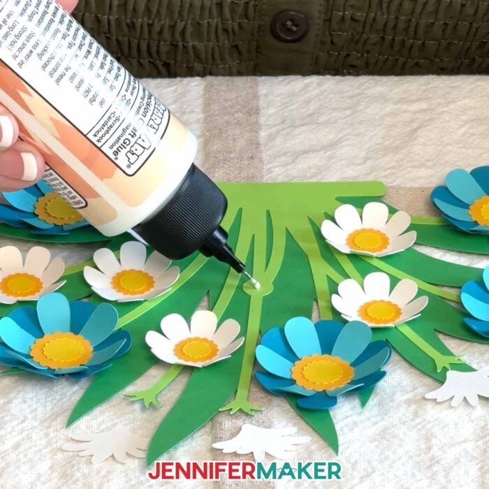 Jennifer glues blue and white flowers onto her flower bouquet lantern's leaves.
