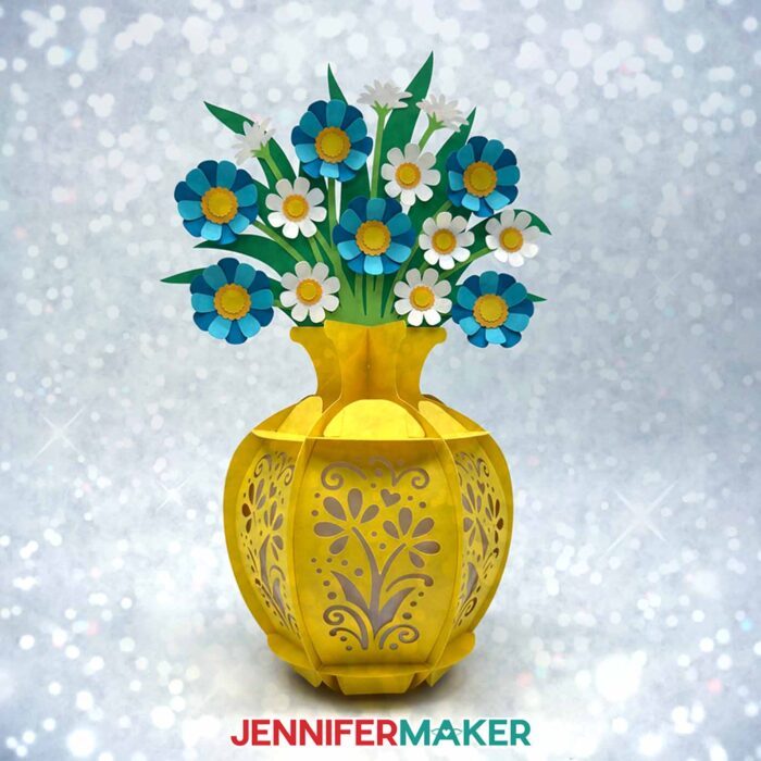A yellow cardstock lantern with a floral vase, blue flowers, and white flowers. Flower Bouquet Lantern design by JenniferMaker.
