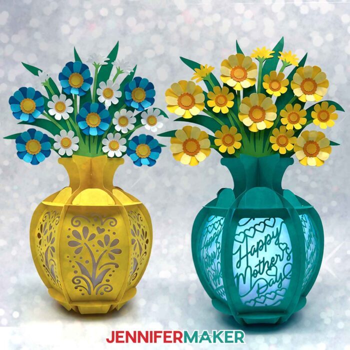 A yellow cardstock lantern with a floral base, blue flowers, and white flowers beside a teal cardstock lantern with a "Happy Mother's Day" base and yellow flowers. Flower Bouquet Lantern design by JenniferMaker.