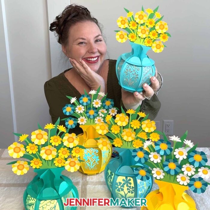 Jennifer holds a blue lantern with yellow flowers, with a variety of other lanterns on a table in front of her.