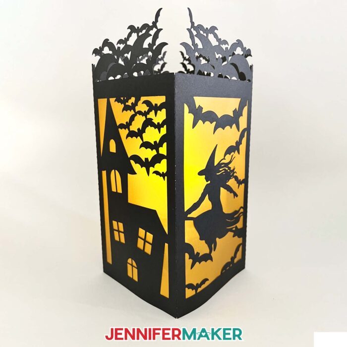 Black Halloween paper lantern showing the other two panels with a haunted house, witch, and bats with orange vellum diffusing the light inside.