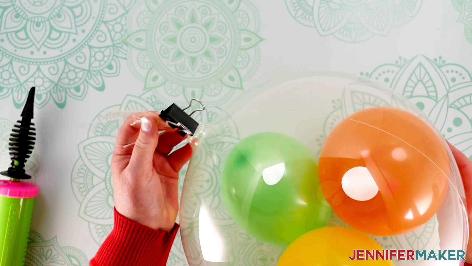 An overhead photo showing an inflated Bobo balloon with a binder clip being attached to the open end to keep the air inside. A hand pump is lying nearby.