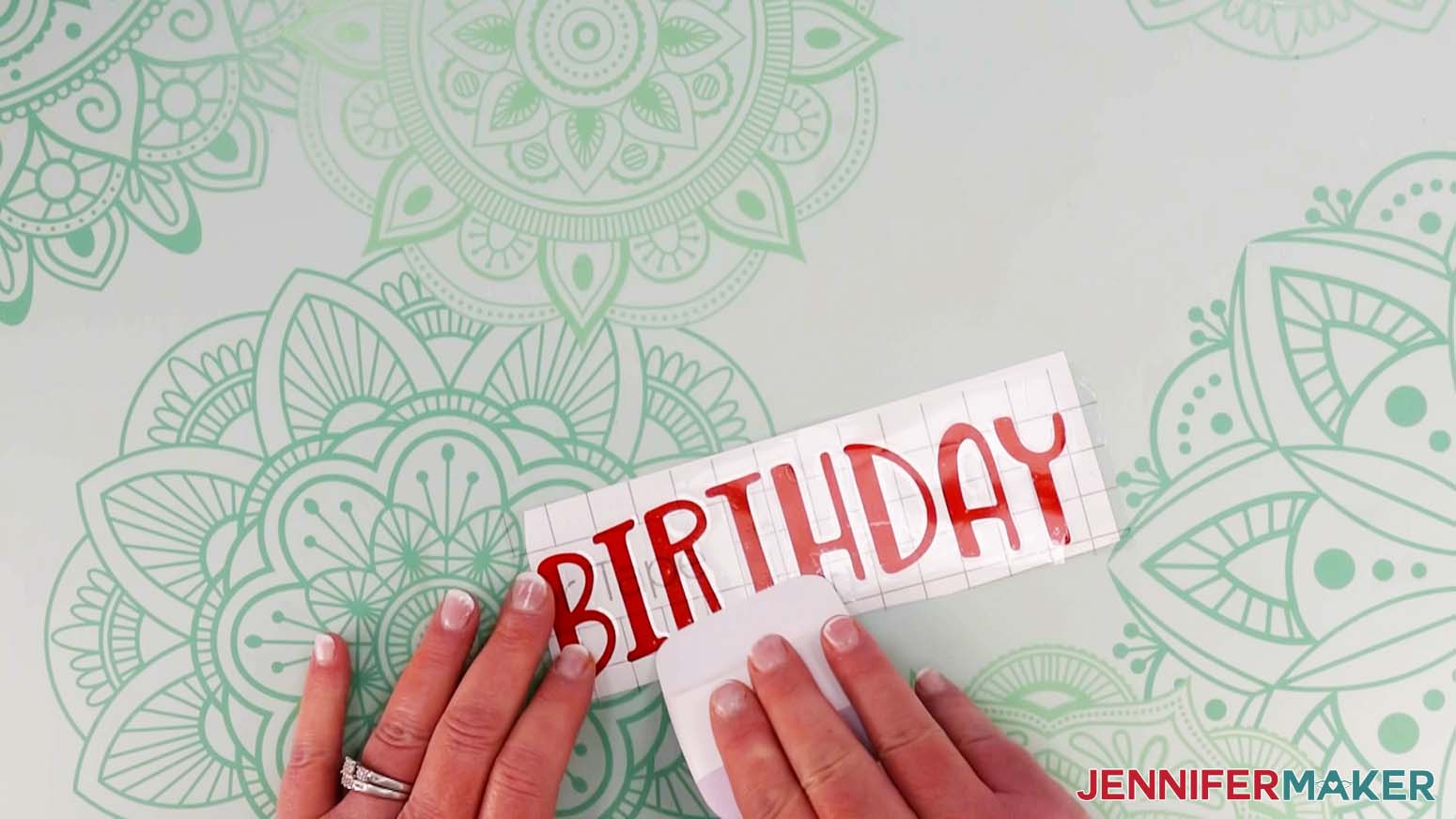 An overhead photo showing a vinyl balloon bouquet decal of the word Birthday with transfer tape cut and applied to the front of the decal with a scraper