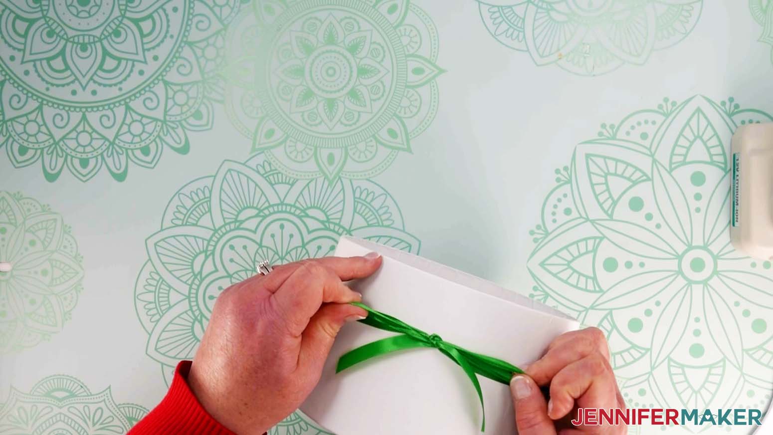 An overhead photo showing two hands tying a bow around a white gift box with green ribbon