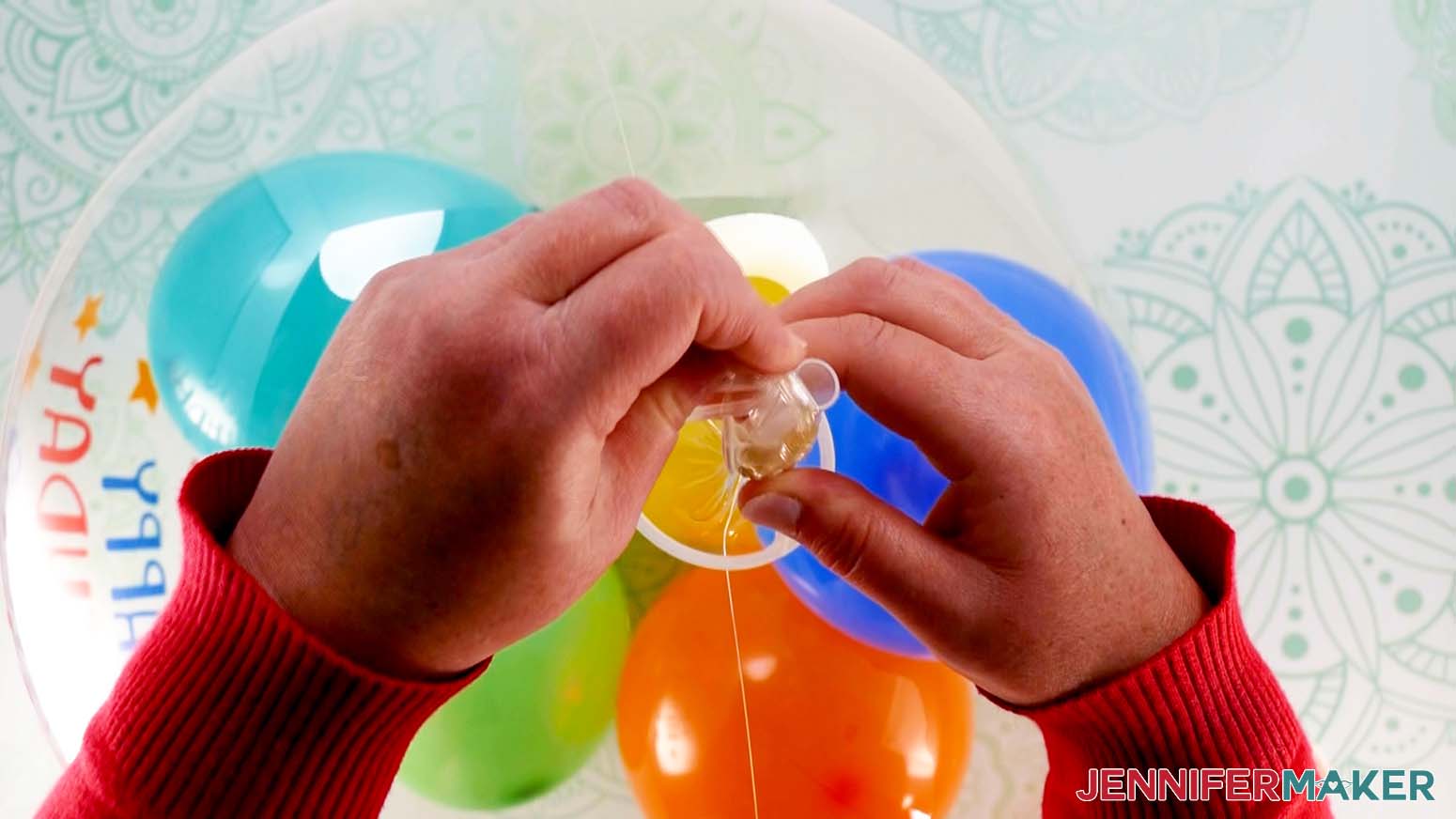 A closeup photo showing a balloon cup being attached to the tied end of an inflated Bobo balloon. Colored latex balloons can be seen inside the balloon.