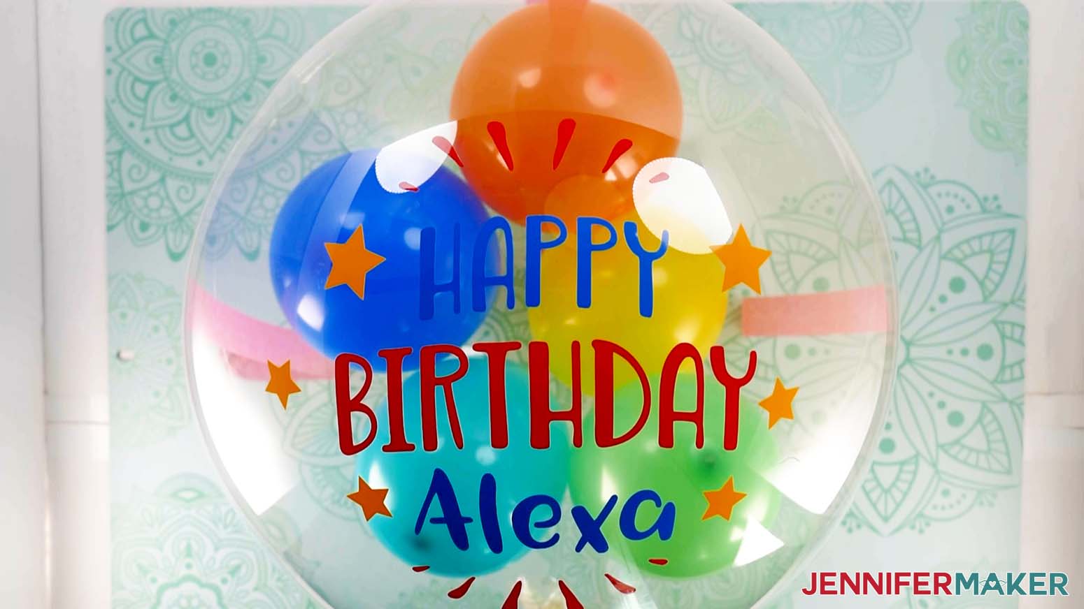 An overhead photo showing a vinyl balloon bouquet decal that says Happy Birthday Alexa applied to an inflated Bobo balloon, which is secured to the work surface below with tape