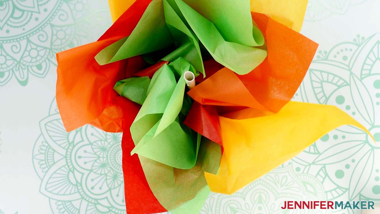 An overhead photo showing a gift box filled with yellow, green, and orange tissue paper and a balloon stick in the center