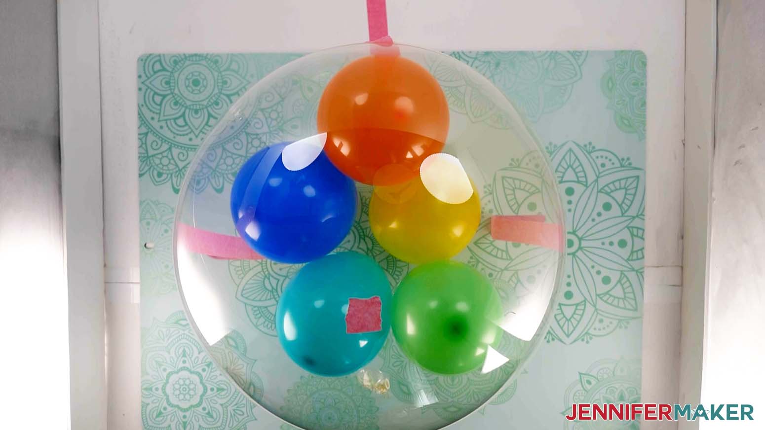 An overhead photo of an inflated Bobo balloon secured to the work surface with a small piece of painter's tape marking the center of the balloon