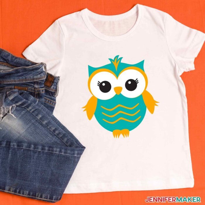 White T-shirt with layered iron-on vinyl of an owl in teal blue, orange, white, and black to teach how to layer vinyl on a shirt