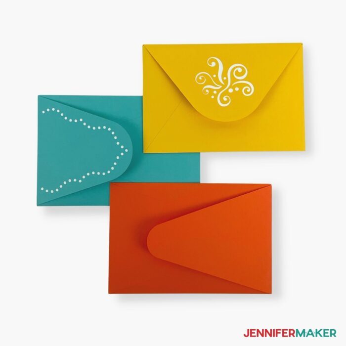 Three rectangular envelopes in yellow, turquoise, and orange with white decorations on white background in the how to make an envelope tutorial.