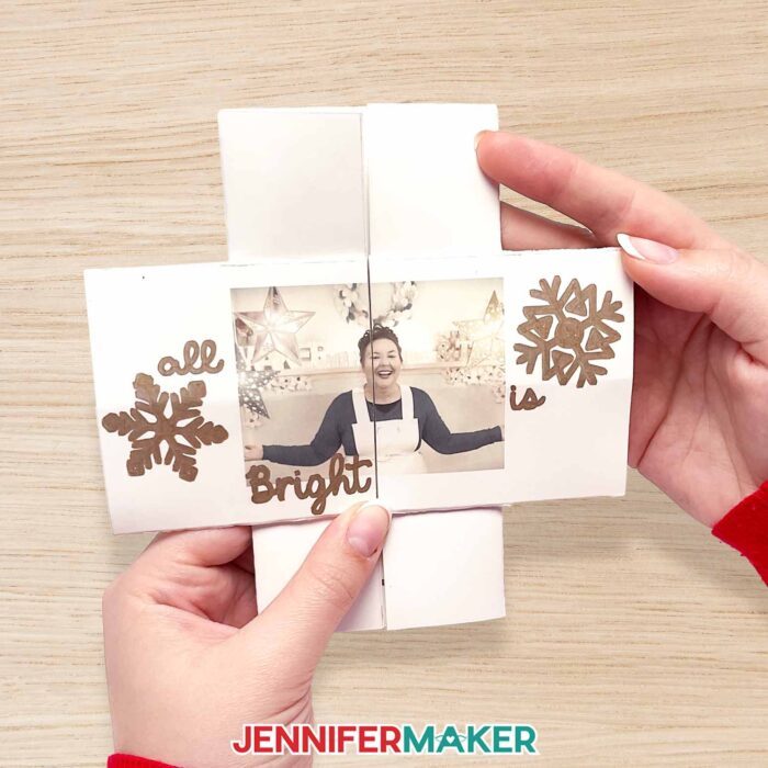 Make a custom infinity card with JenniferMaker's tutorial! Jennifer holds an infinity card open to a "face" of Jennifer smiling in her studio! Around her are snowflakes and a sentiment "All Is Bright" written in copper pen.