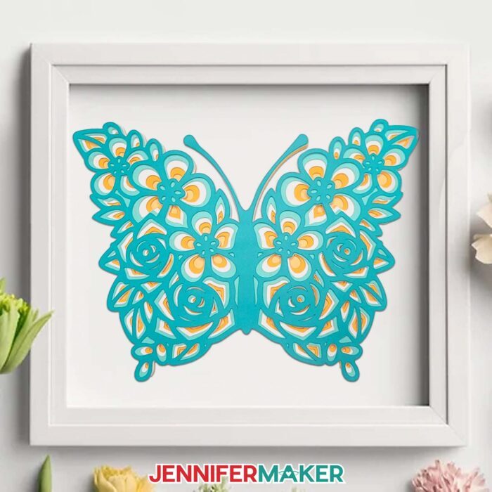A layered teal and yellow cardstock butterfly is displayed in a shadow box. Layered floral butterfly Design by JenniferMaker.