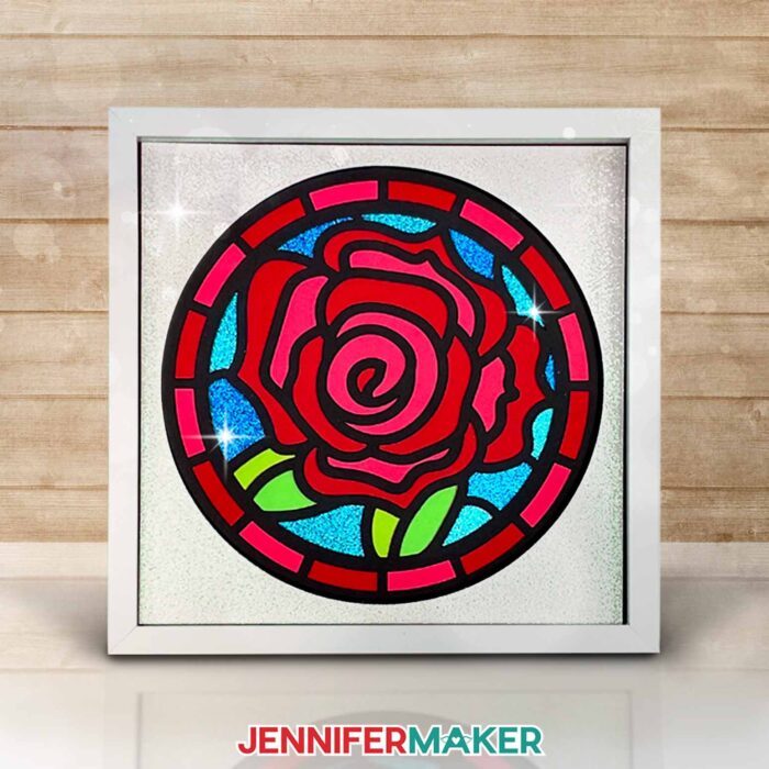 Make layered paper stained glass windows with Jennifer Maker's tutorial! Image shows a colorful rose stained glass shadowbox in a white frame.
