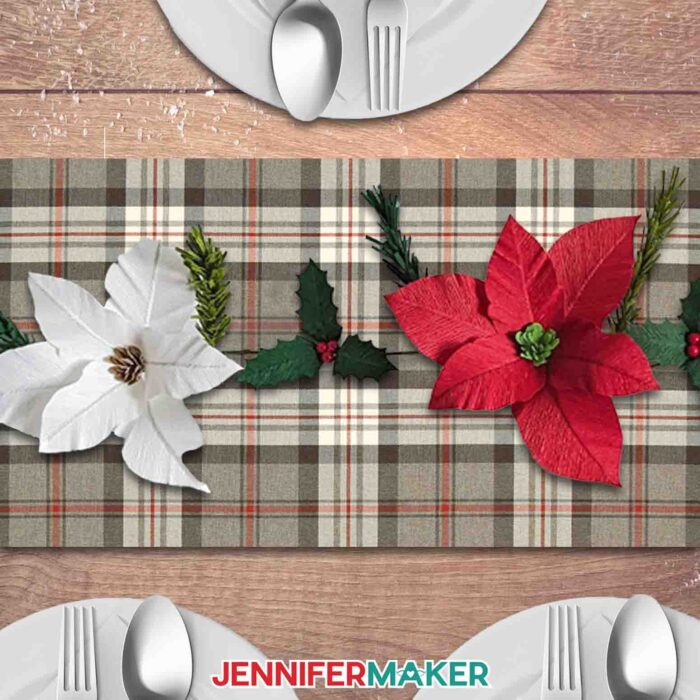 Learn to make a crepe paper floral garland with JenniferMaker's tutorial! A crepe paper garland of poinsettias, holly, and pine sprigs lays displayed on a backdrop of holiday plaid fabric, with place settings surrounding it.