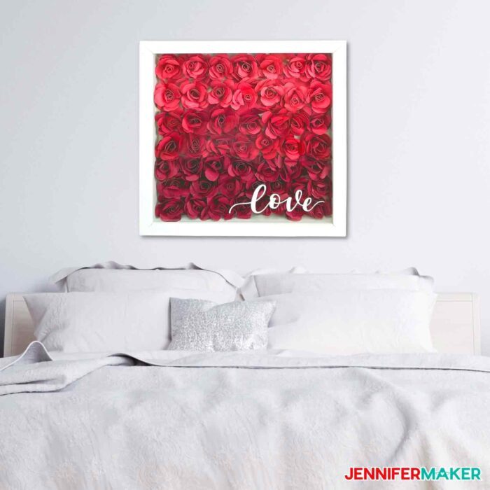 Paper Flower Shadow Box with red roses and a white vinyl "love" hand lettered design on the glass in a white bedroom