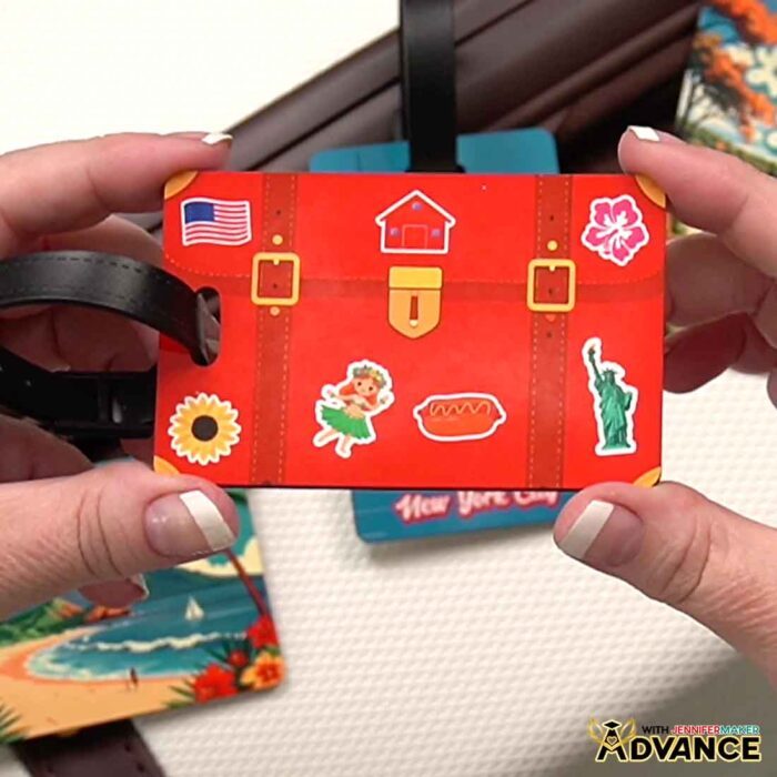 Hands hold a customized luggage tag decorated like a suitcase with different "stickers"on it. Learn how to custom Make A QR Code With Canva in the Advance with JenniferMaker tutorial