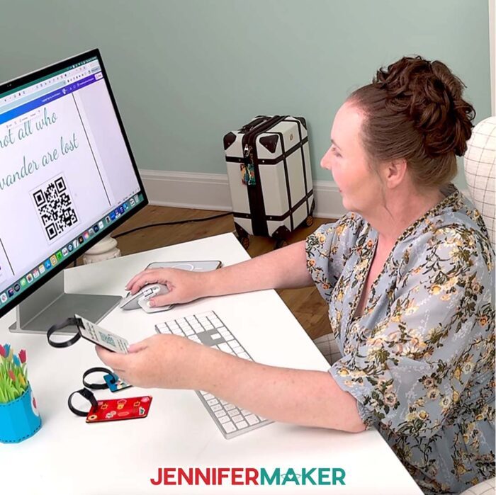 Jennifer Maker sits at her computer desk, designing a QR code luggage tag in Canva. Learn how to Make A QR Code With Canva in the free tutorial