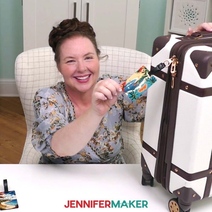 Jennifer Maker shows off a sublimation luggage tag on a suitcase at her craft table. Learn about these and more of the Best Sublimation Blanks in her free blog post