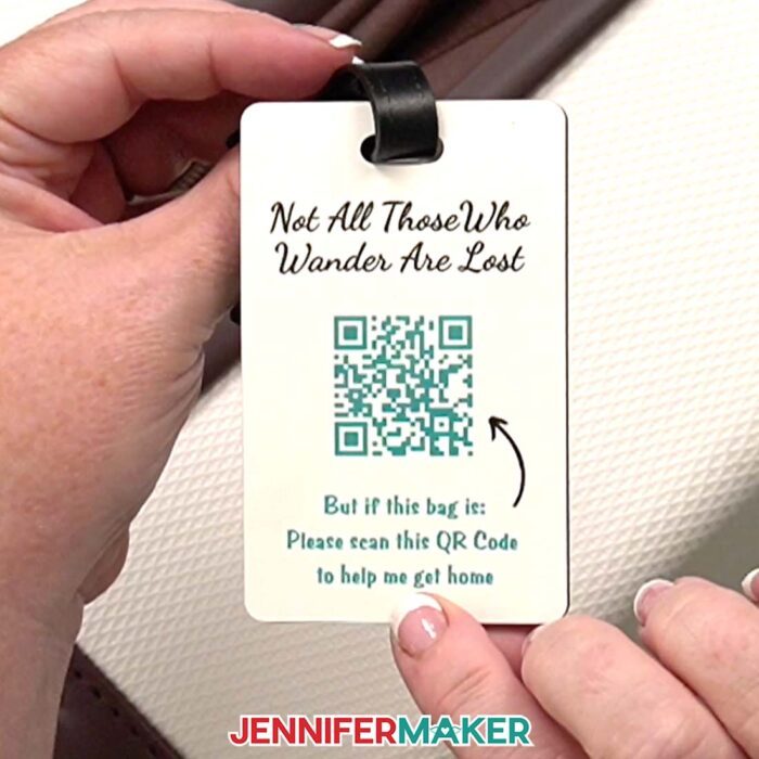 Hands hold a luggage tag with a QR code that says "Not All Those Who Wander Are Lost" at the top and "But if this bag is: Please scan this QR Code to help me get home" at the bottom. Learn how to Make A QR Code With Canva in the free tutorial
