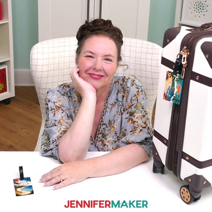 Jennifer Maker sits at her craft table among luggage tag crafts, smiling. Learn how to Make A QR Code With Canva in the free tutorial