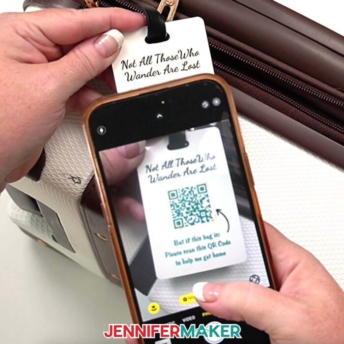Hands hold a phone that is scanning a QR code that says "Not All Those Who Wander Are Lost" at the top and "But if this bag is: Please scan this QR Code to help me get home" at the bottom. Learn how to Make A QR Code With Canva in the free tutorial