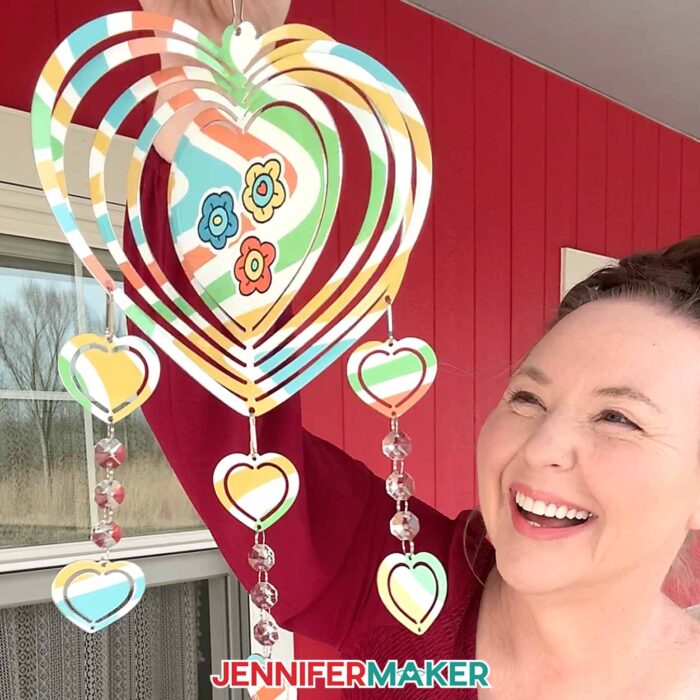 Jennifer holding up a heart-shaped wind spinner with six smaller heart-shaped dangles. The spinner has colorful swirls for the background and flowers in the center.