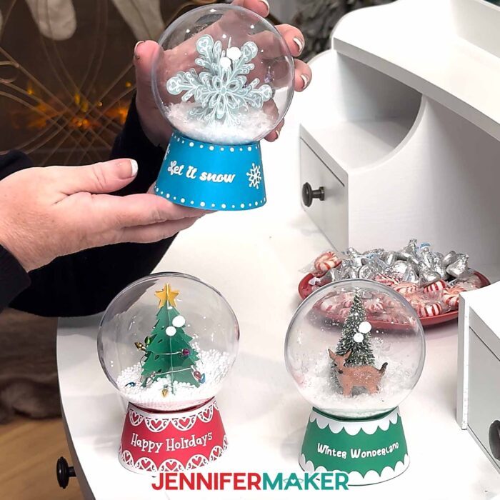 Hands show off three different Snow Globe Gift Box projects in red, green, and blue over a white desk