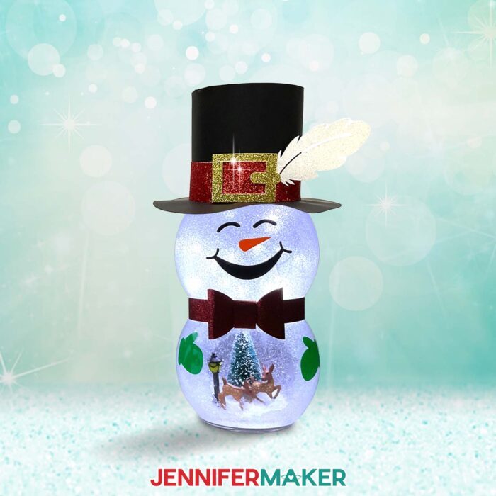 A cute smiling Snowman With Belly Scene of deer and a cardstock feather in his hat sits on display, all lit up with a wintry backdrop