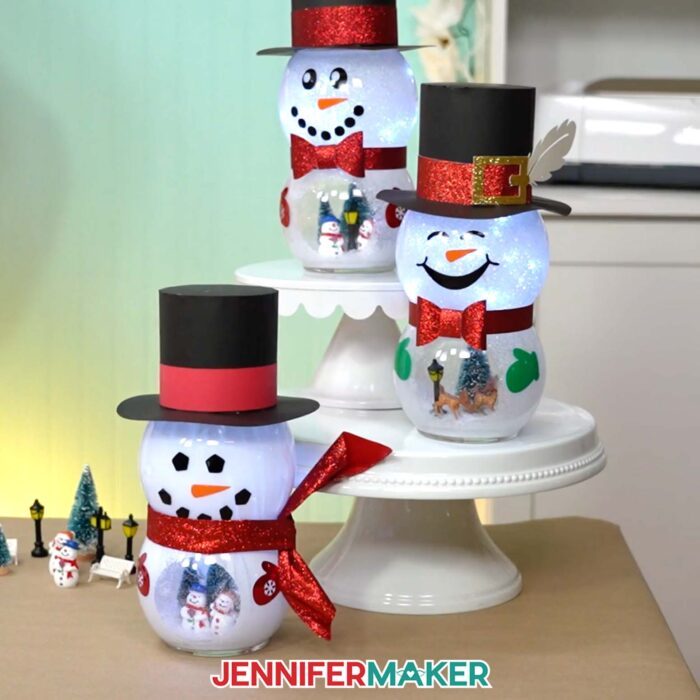 Three Snowman With Belly Scene projects sit on display on Jennifer's craft table, each with different faces, scenes, and accessories