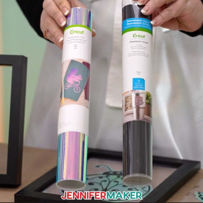Jennifer holds up rolls of Cricut blue holographic vinyl and Cricut black premium vinyl for making window clings.