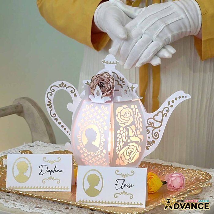 A cardstock teapot lantern sits on a tea tray with matching name place cards set in front, one for Daphne and one for Eloise.