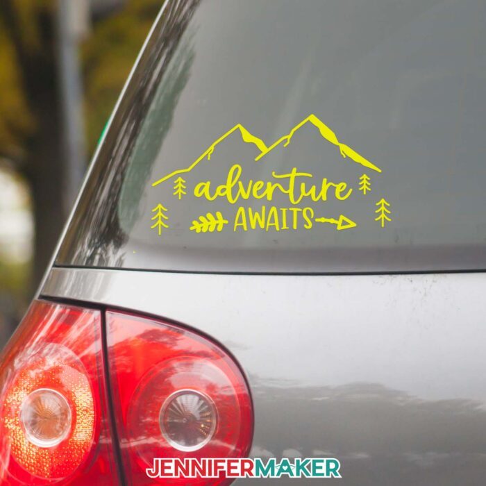 A yellow vinyl car decal reading Adventure Awaits with mountains on the back window of a car.