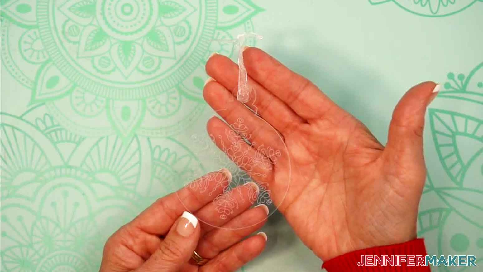 A hand is holding the completed engraved acrylic ornament up so you can see the intricate engraved design.