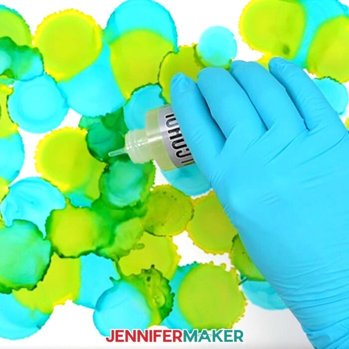 A close up demonstration of applying an alcohol ink blending agent to an Alcohol Ink On Paper project with blues and greens